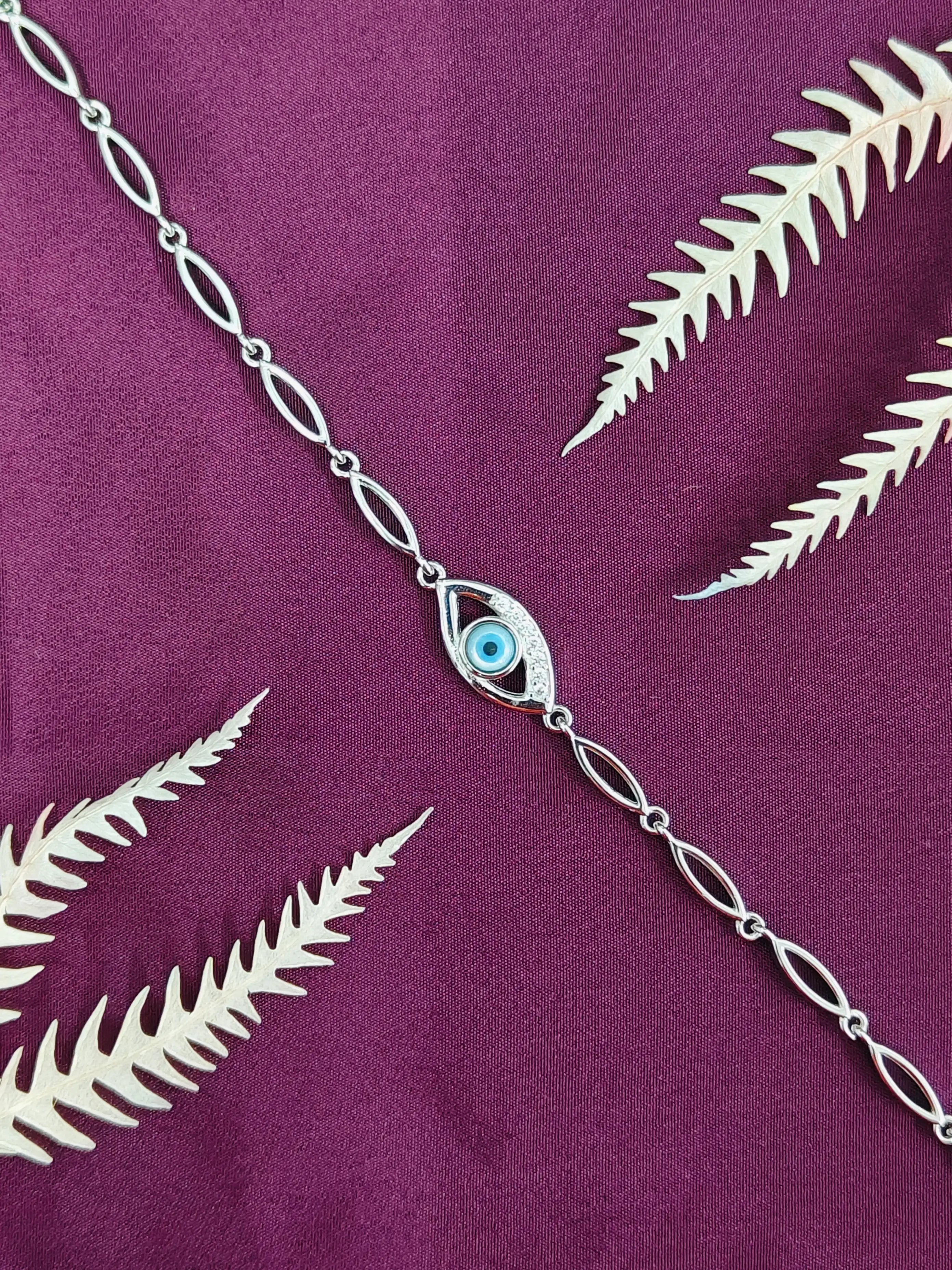 Silver chain necklace with an eye-shaped pendant on a purple fabric background